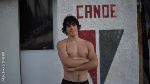Portrait of handsome attractive shirtless athletic young man with arms crossed after canoeing training looking at camera by the sports club in summer. Cine lens.