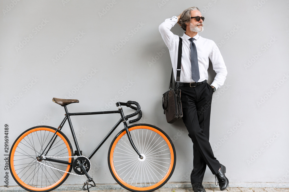 Photo of satisfied old businessman standing with bicycle Photo of satisfied old businessman standing with bicycle