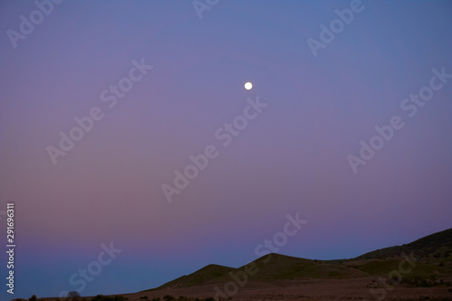 Landscape hills view with little full moon at the evening multicolored sky. Bright colors. 