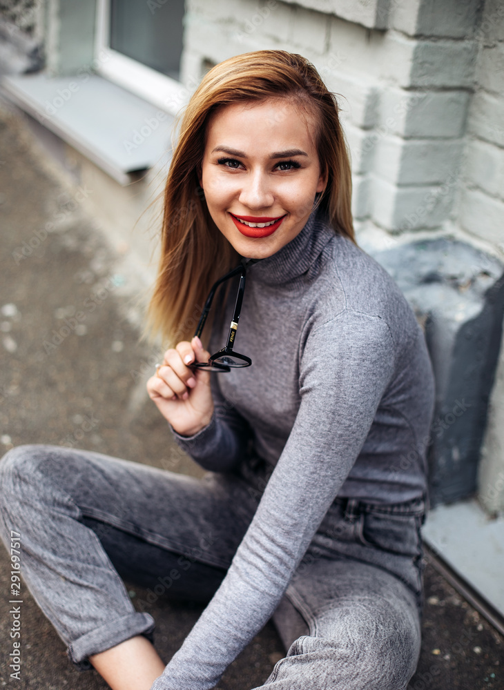 Fototapeta premium Close up fashion street stile portrait of young stylish girl student wearing boyfriend jeans, white sneakers and gray jeans.Pretty laughing girl has a good time in autumn weekend