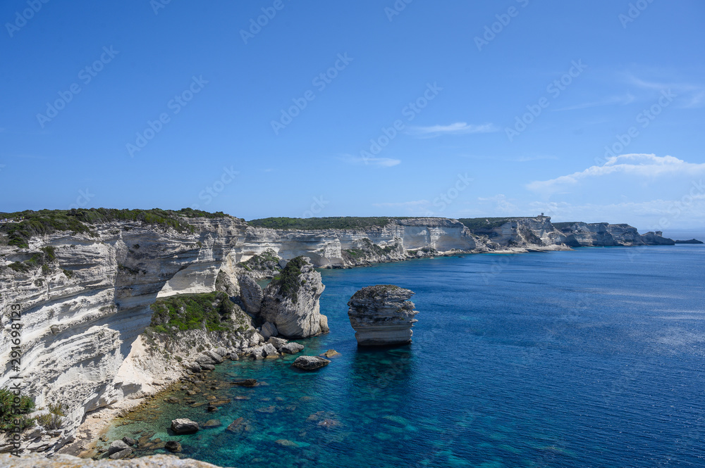 Panoramic view of Bonifacio Corsica on white limestone cliffs with a single rock nearby. Sea and blue sky with clouds