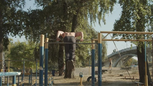 Wallpaper Mural Shirtless motivated strong athlete with perfect trained body doing gymnastic exercises on crossbar while working out in outdoor gym at sunset. Muscular man training doing backflip on horizontal bar. Torontodigital.ca