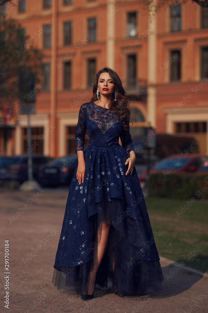 Elegant woman in blue ball gown dress standing and posing on a sunny evening at city street. Fashion model full length portrait Elegant woman in blue ball gown dress standing and posing on a sunny evening at city street. Fashion model full length portrait