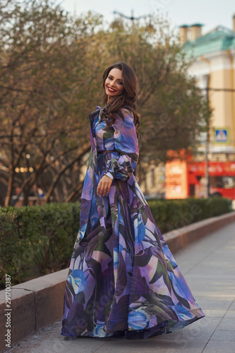 Outdoor fashion style portrait of young tall slim woman in colorful blue chifon dress walking city street. Full length portrait © Dmitry Tsvetkov