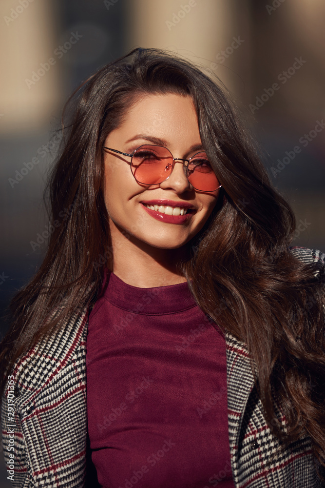 Face portrait of pretty girl walking in city on a sunny spring or autumn day. Smiling woman with long brown wavy hair. Face portrait of pretty girl walking in city on a sunny spring or autumn day. Smiling woman with long brown wavy hair.