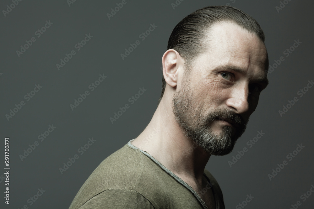 Male beauty concept. Fabulous at any age. Portrait of 45-year-old man  standing over dark gray background. Hair brushed back. Rocker, biker style.  Scar on forehead. Close up. Copy-space. Studio shot Stock Photo |