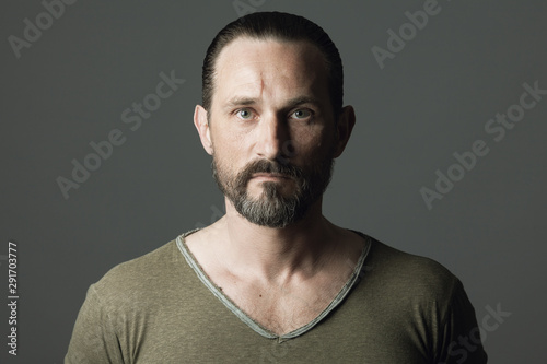 Male beauty concept. Fabulous at any age. Portrait of 45-year-old man standing over dark gray background. Hair brushed back. Rocker, biker style. Scar on forehead. Close up. Text space. Studio shot