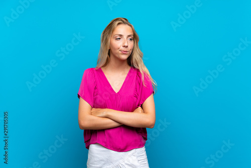 Blonde young woman over isolated blue background with confuse face expression © luismolinero