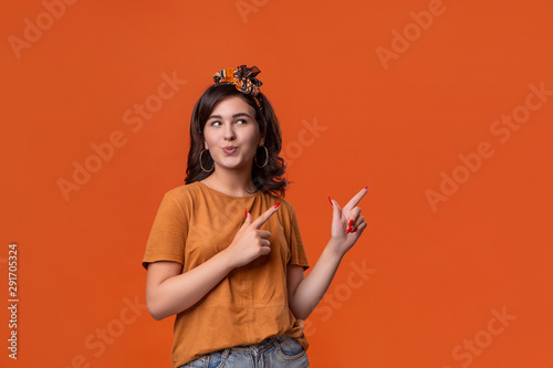Pretty brunette woman in a t-shirt and beautiful headband pointing with her fingers at the rights side isolated over orange background. Place for ad.