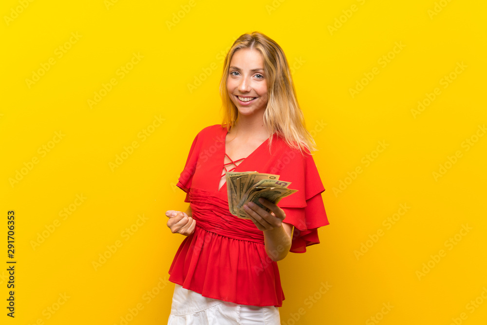 Blonde young woman over isolated yellow background taking a lot of money Blonde young woman over isolated yellow background taking a lot of money