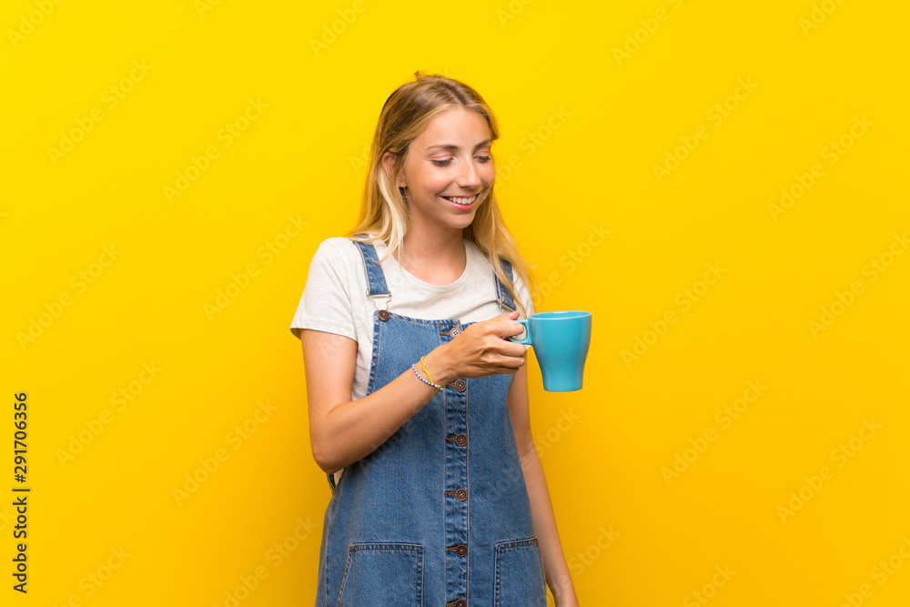 Blonde young woman over isolated yellow background holding hot cup of coffee Blonde young woman over isolated yellow background holding hot cup of coffee