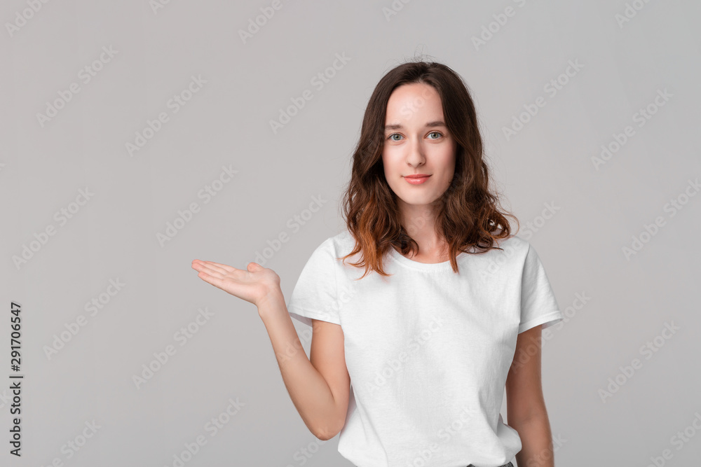 Pretty brunette woman in a white tee holding palm of a hand with empty space for product placement standing isolated over grey background. Pretty brunette woman in a white tee holding palm of a hand with empty space for product placement standing isolated over grey background.