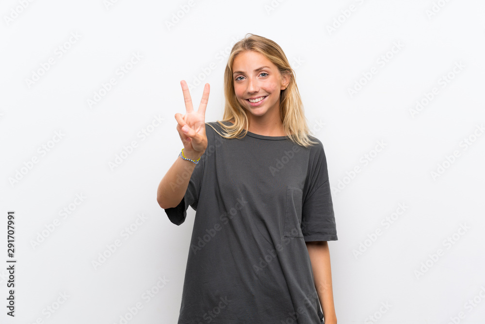 Blonde young woman over isolated white background smiling and showing victory sign Blonde young woman over isolated white background smiling and showing victory sign