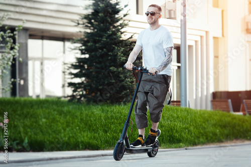 Attractive man riding electric kick scooter at cityscape background.