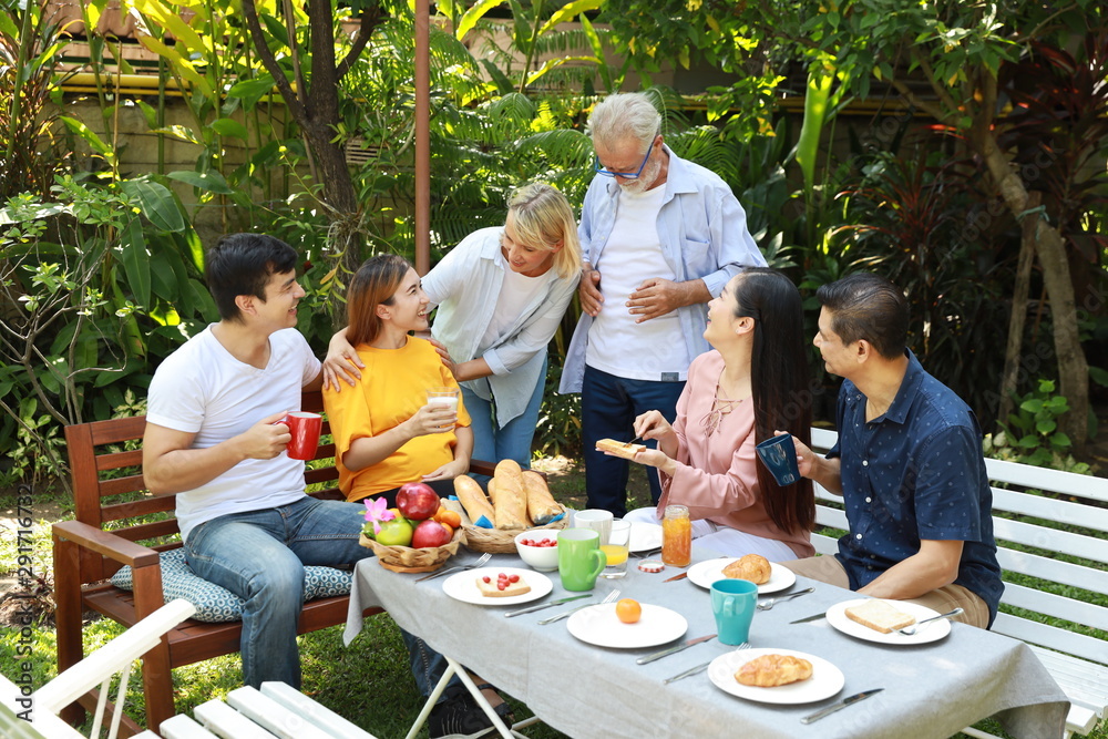 Happy multiethnic family sitting at a breakfast table in backyard outdoor on sunny day with smiling face.