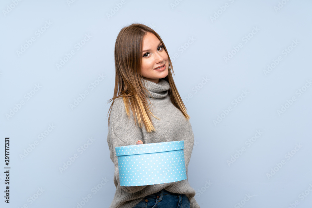 Fototapeta premium Teenager girl with sweater over isolated blue background holding gift box