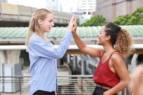 close up two caucasian businesswomen doing give me five together meaning of teamwork while walking on walk way with city and skytrain background