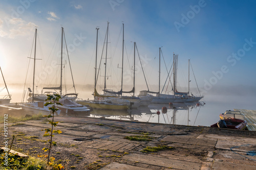 Autumnal mist on a river with yachts and boats anchored in harbor,  at dawn, ...