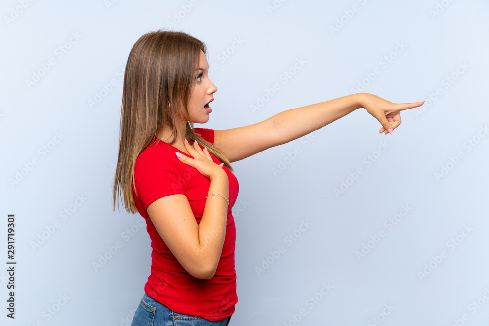 Teenager girl over isolated blue background pointing finger to the side Teenager girl over isolated blue background pointing finger to the side