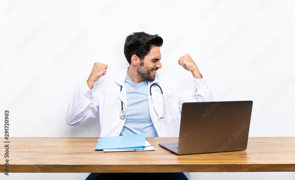 Young doctor man with his laptop over isolated wall celebrating a victory Young doctor man with his laptop over isolated wall celebrating a victory