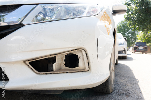 Damage to the front left bumper of a white sedan, Caused by accident.