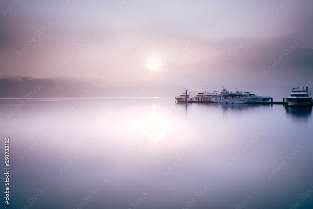 Beautiful tranquil landscape at Sun Moon lake in Nantao, Taiwan. Pier with boats and background of foggy mountains. Concept of peaceful, traanquility of nature.