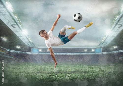 Soccer player on a football field in dynamic action at summer day under sky with clouds. Sporty man is shooting the ball outdoor. Sport, game concept.