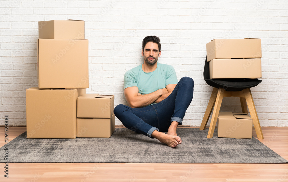 Handsome young man moving in new home among boxes keeping arms crossed Handsome young man moving in new home among boxes keeping arms crossed