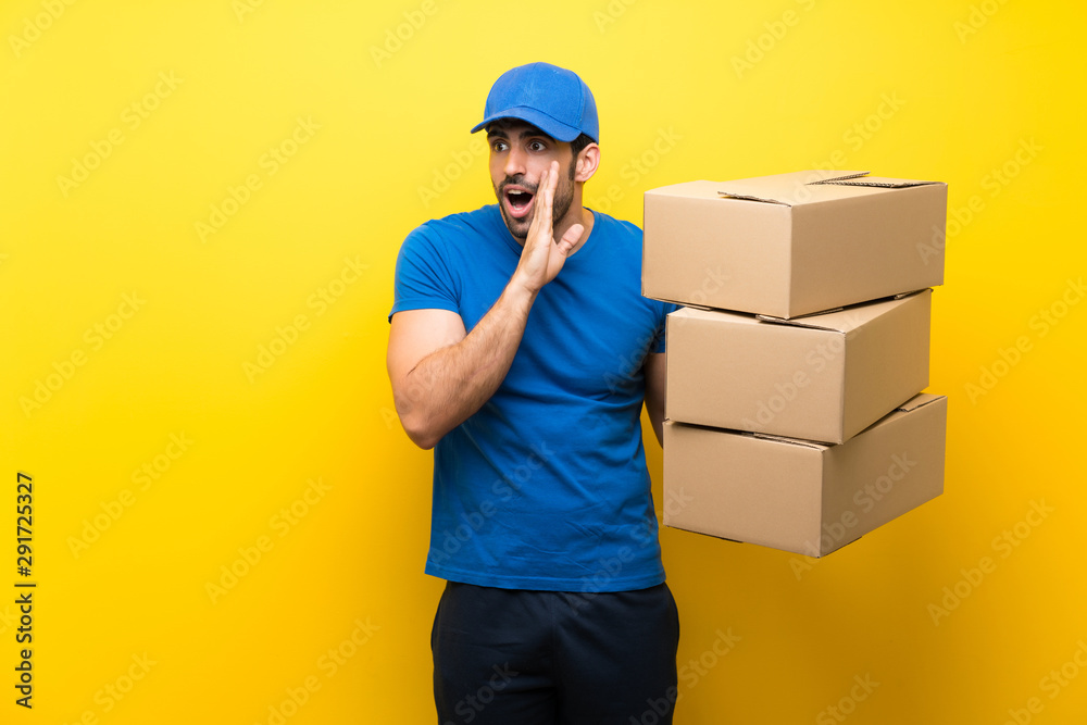 Young delivery man over isolated yellow wall whispering something Young delivery man over isolated yellow wall whispering something