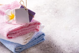 Lots of colorful bath towels stacked on each other with hand soap and flower on light stone background, copy space