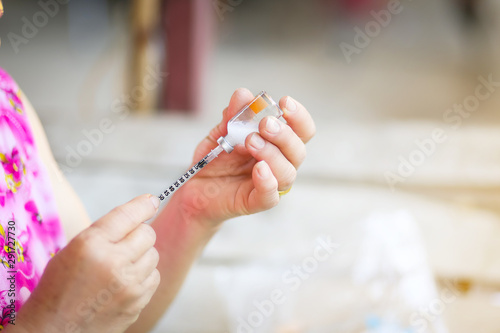Close up of old female hand making subcutaneous insulin injection into a diabetes patient abdomen with insulin syringe at home.   photo