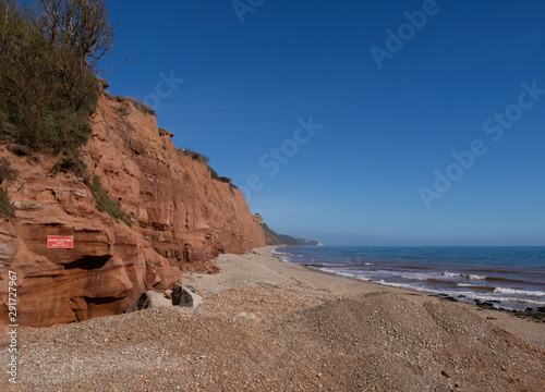 The famous Jurassic Coast red cliffs at Sidmouth, Devon, England. Looking East from Sidmouth Beach with warning of danger of landslides.