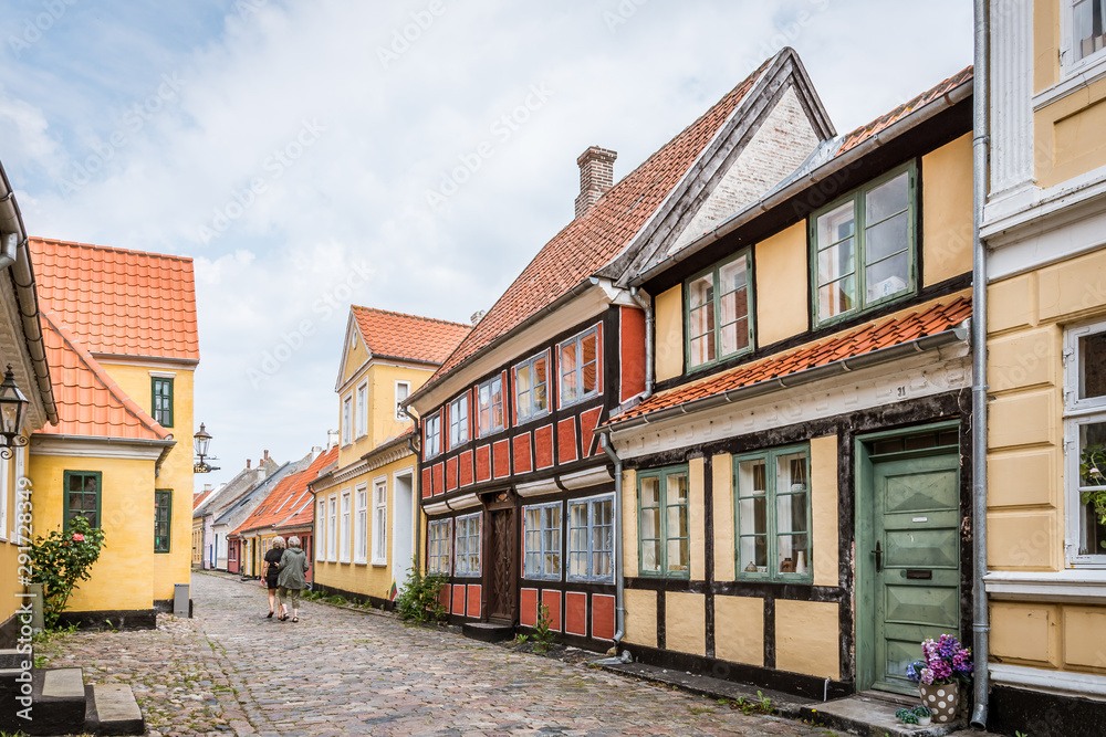 two persons walking at the end of an idyllic cobblestone street with old half timbered houses