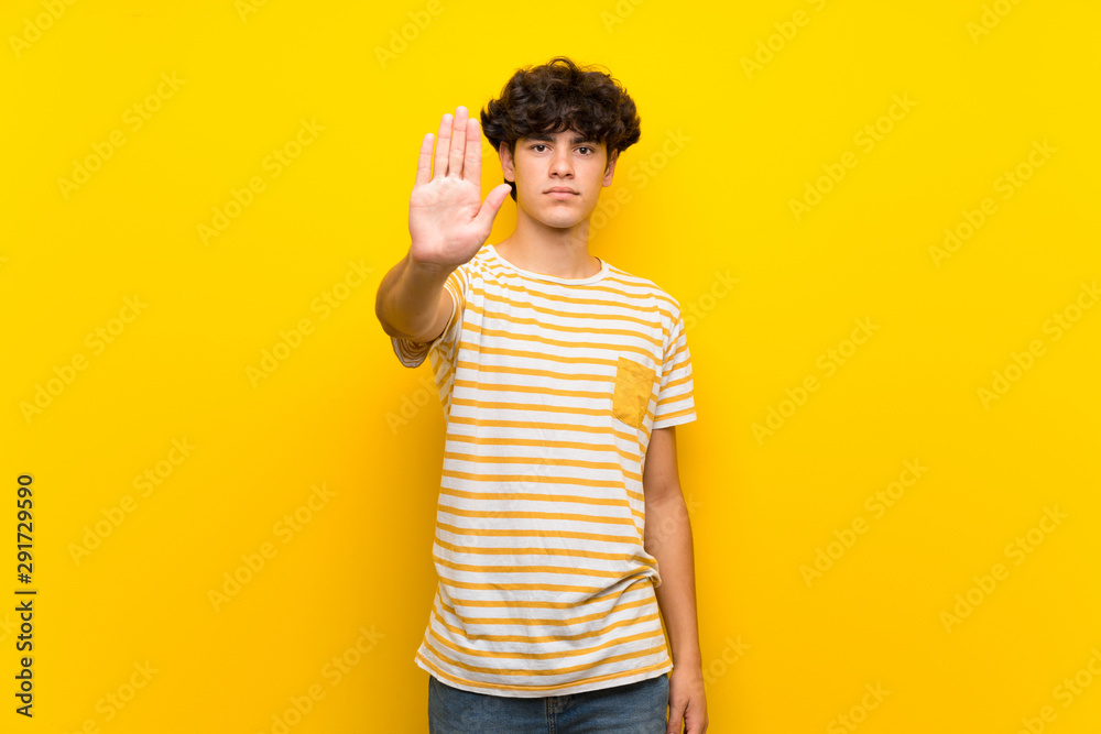 Young man over isolated yellow wall making stop gesture Young man over isolated yellow wall making stop gesture