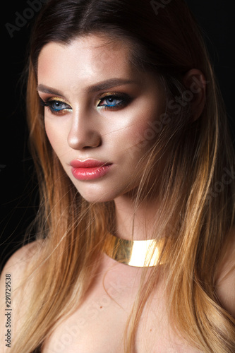 Young attractive model with the professional colorfull make-up, bright blue eyes and arrows and gold necklace.