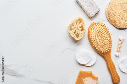top view of cotton pads, ear sticks, loofah, pumice stone, face sponge and hair brush on marble surface