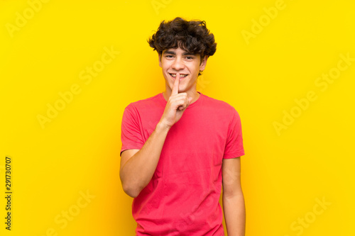 Young man over isolated yellow wall doing silence gesture