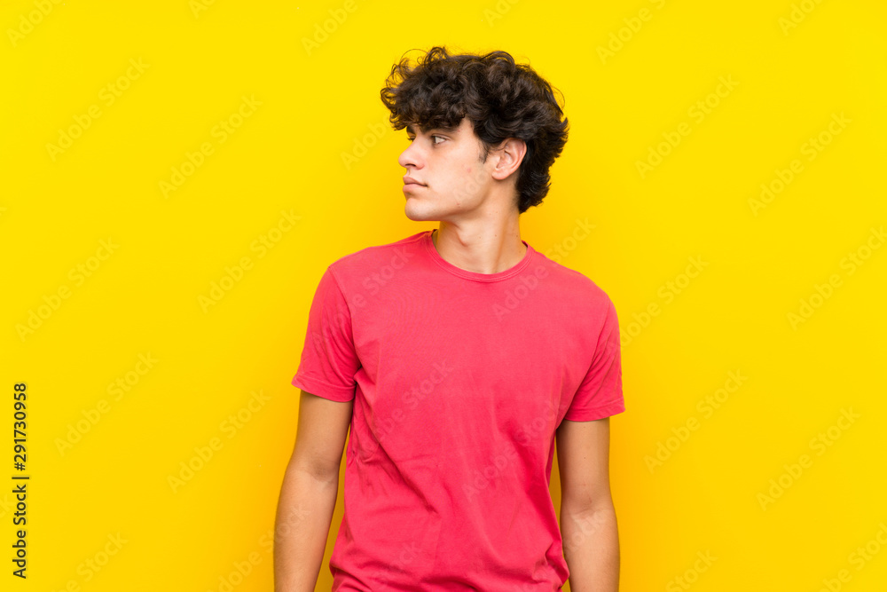 Young man over isolated yellow wall looking side Young man over isolated yellow wall looking side