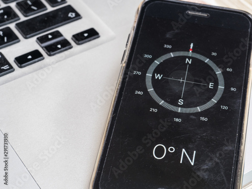 A compass on a smart phone indicates zero degrees North. Other compass points are seen blurring into distance. The phone sits on the corner of a computer keyboard.Technology  photo