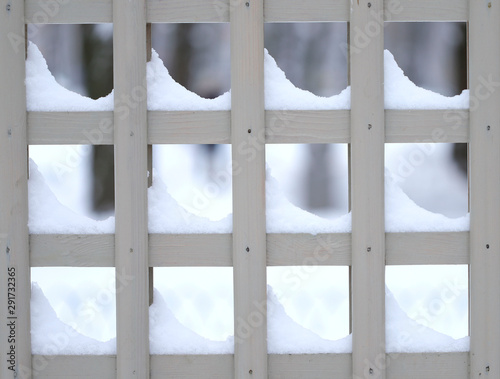 Abstract winter background. Fragment of a wooden painted pergola with snowdrifts. Side view, close-up. Concept of the seasons.