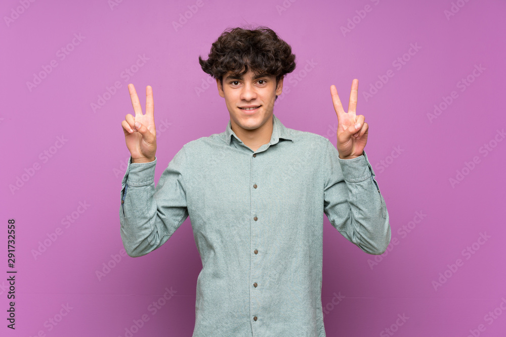 Young man over isolated purple wall showing victory sign with both hands Young man over isolated purple wall showing victory sign with both hands