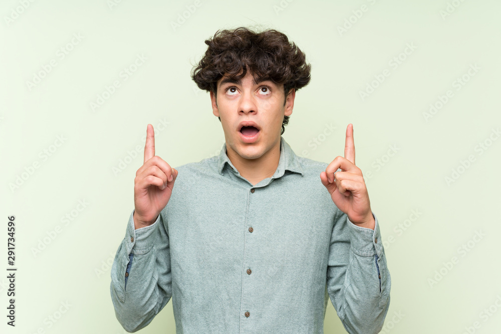 Young man over isolated green wall pointing with the index finger a great idea Young man over isolated green wall pointing with the index finger a great idea