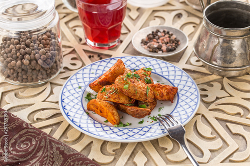 Baked unpeeled potato wedges on white plate and glass of red drink on oriental wooden table