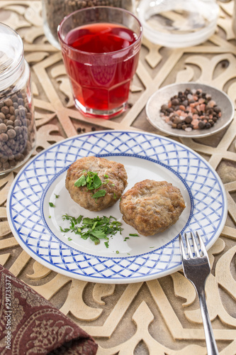 Meat patties on white plate with glass of red drink on oriental wooden table