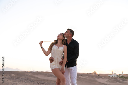 Young romantic couple in elegant clothes standing among the desert hugging and looking at the upper left corner