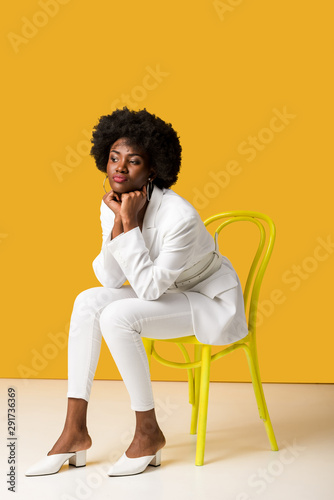 sad african american girl sitting on yellow chair on orange © LIGHTFIELD STUDIOS