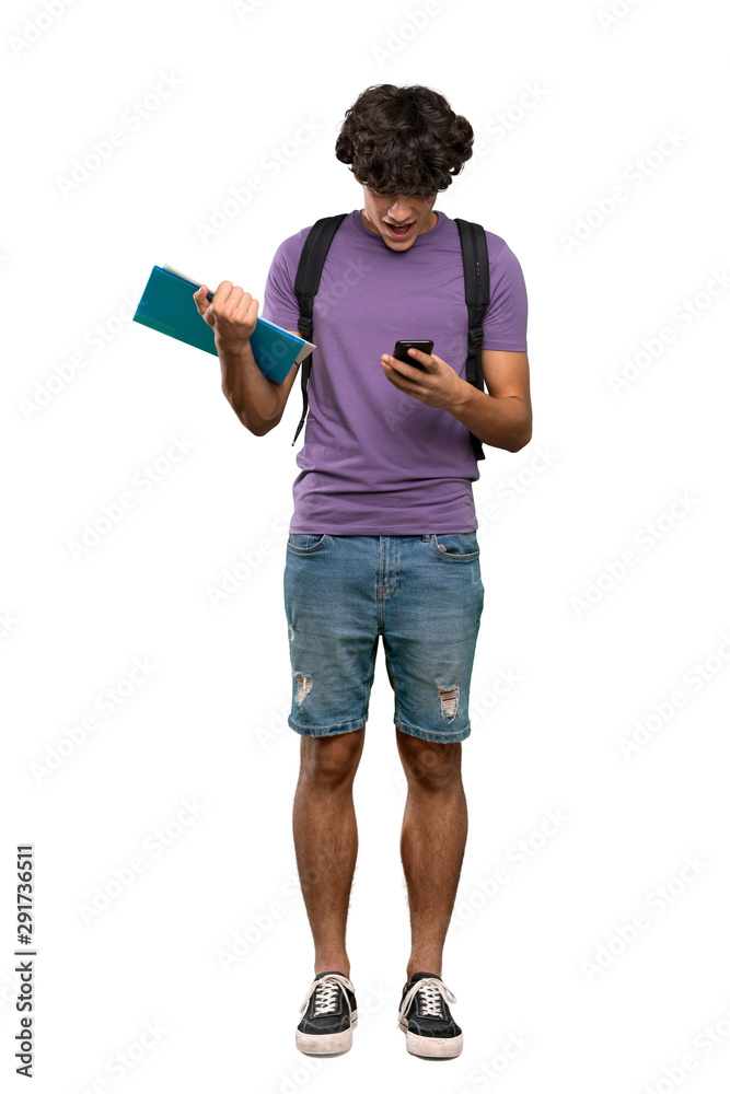 A full-length shot of a Young student man surprised and sending a message over isolated white background