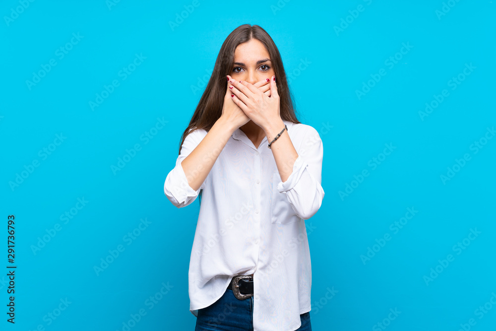 Young woman over isolated blue background covering mouth with hands Young woman over isolated blue background covering mouth with hands