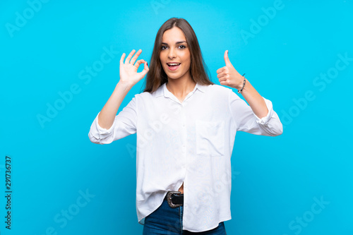 Young woman over isolated blue background showing ok sign and thumb up gesture