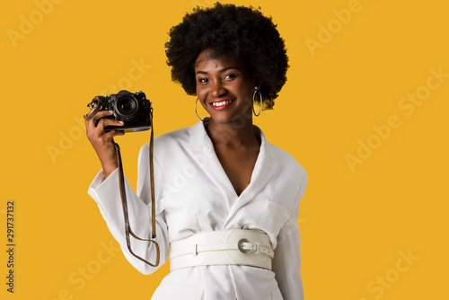 happy african american woman holding digitla camera isolated on orange photo